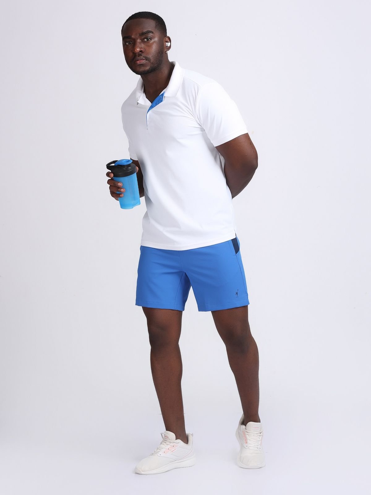 Full-body pose of a man wearing royal blue RacerStrip Performance shorts and a white polo, holding a shaker bottle.